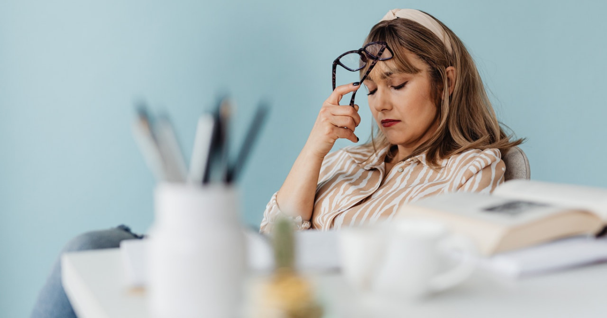 significato e sintomi dell'astenia - primo piano di donna in ufficio stanca, con occhi chiusi e occhiali da vista in mano