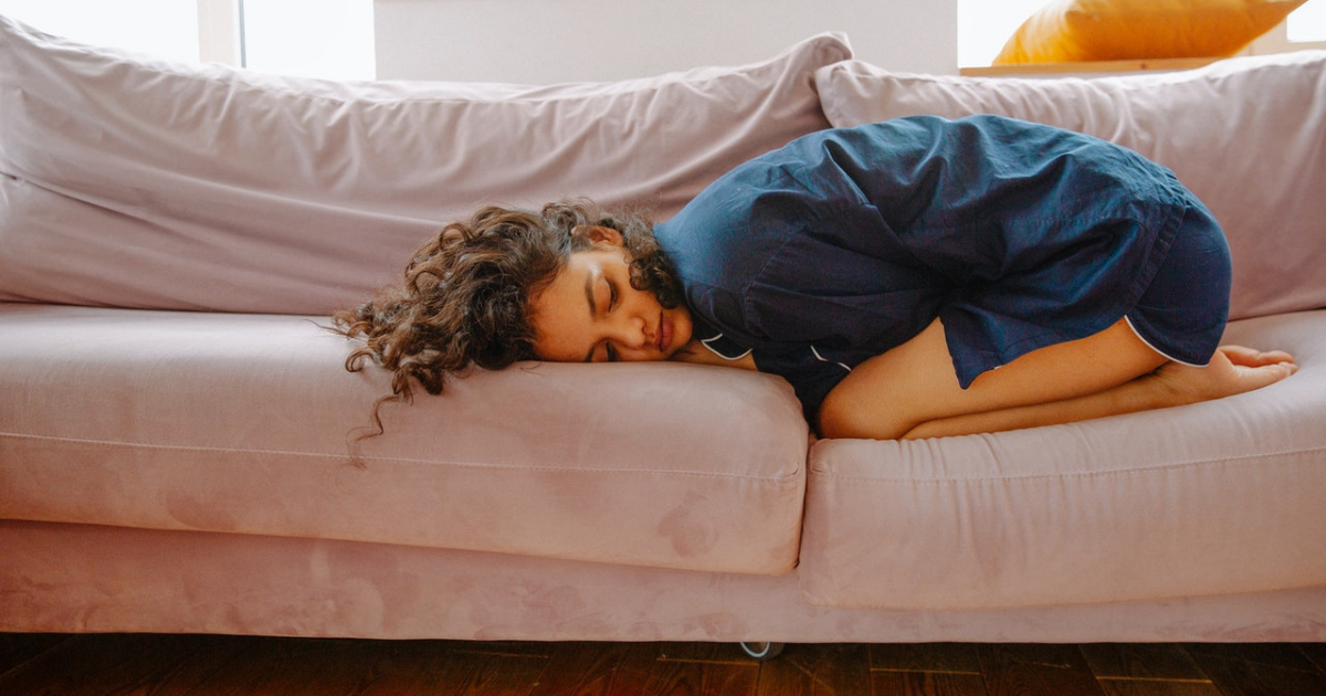 magnesio e sindrome premestruale - donna rannicchiata sul divano con mal di pancia e mal di testa