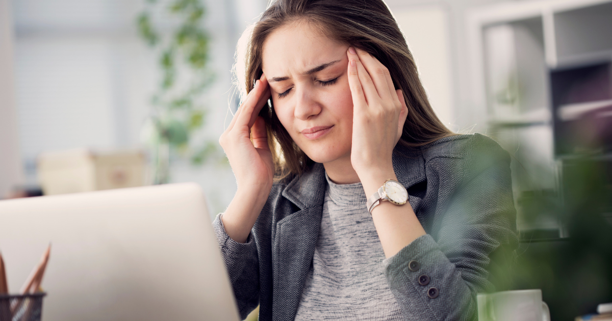 magnesio e mal di testa - ragazza davanti al pc con occhi chiusi e mani che massaggiano le tempie